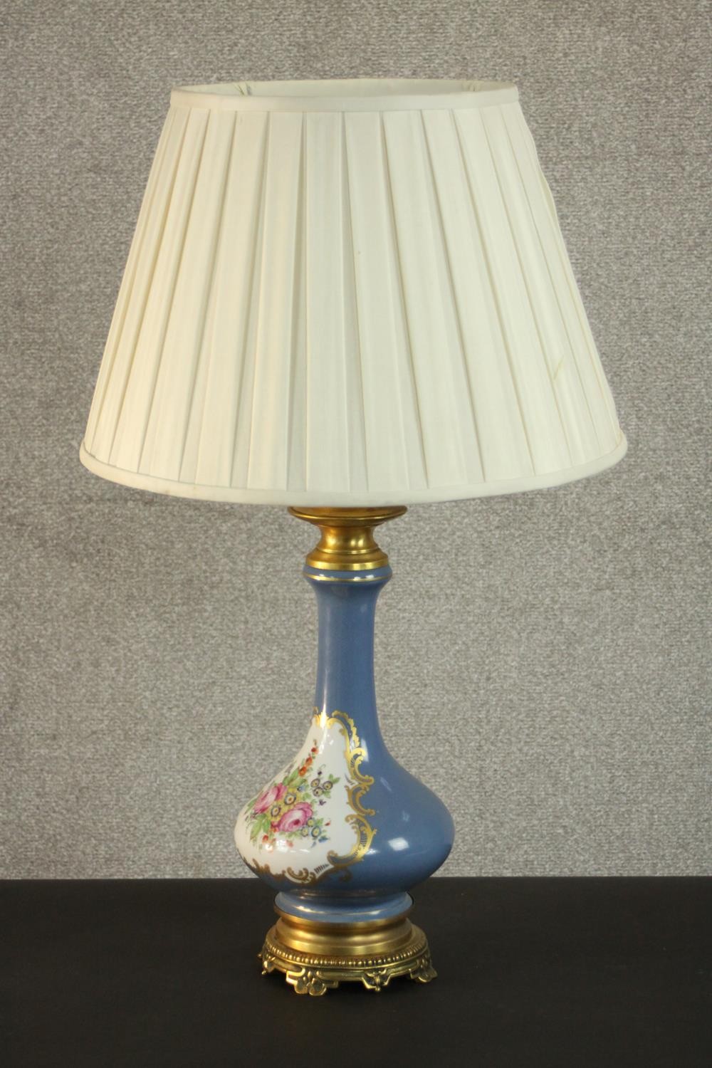 A hand painted and gilded porcelain floral design lamp on a gilt metal repousse design stand. H.77