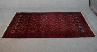 A Persian Meshed rug with repeating lozenge design on a burgundy ground within stylised borders. L.
