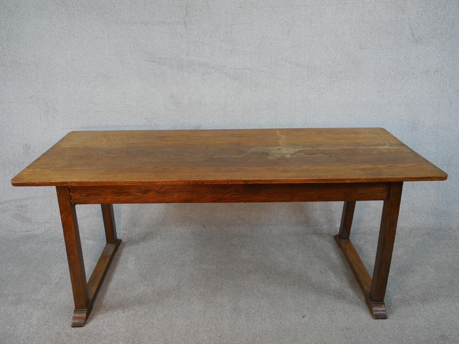 A Heals style Arts and Crafts oak refectory dining table on square trestle supports resting on