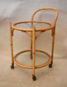 A mid 20th century bamboo drinks trolley, of circular form with two glass tiers. 50cm W x 50cm D x