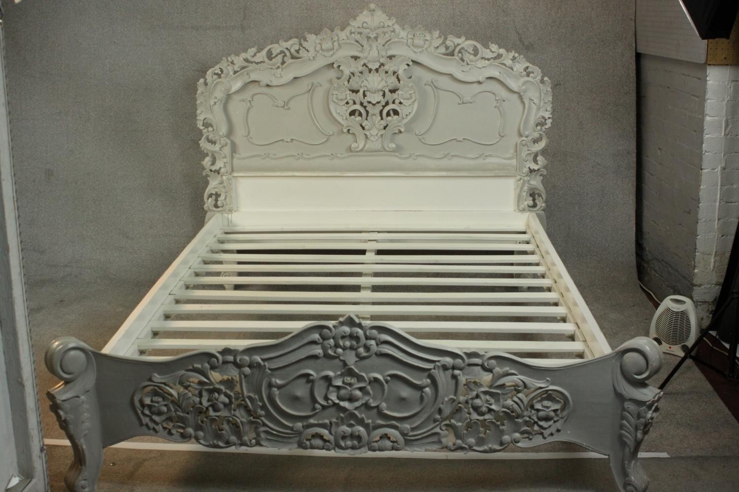 A grey and white painted ornately carved king size bed, the headboard and foot carved and pierced