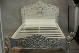 A grey and white painted ornately carved king size bed, the headboard and foot carved and pierced