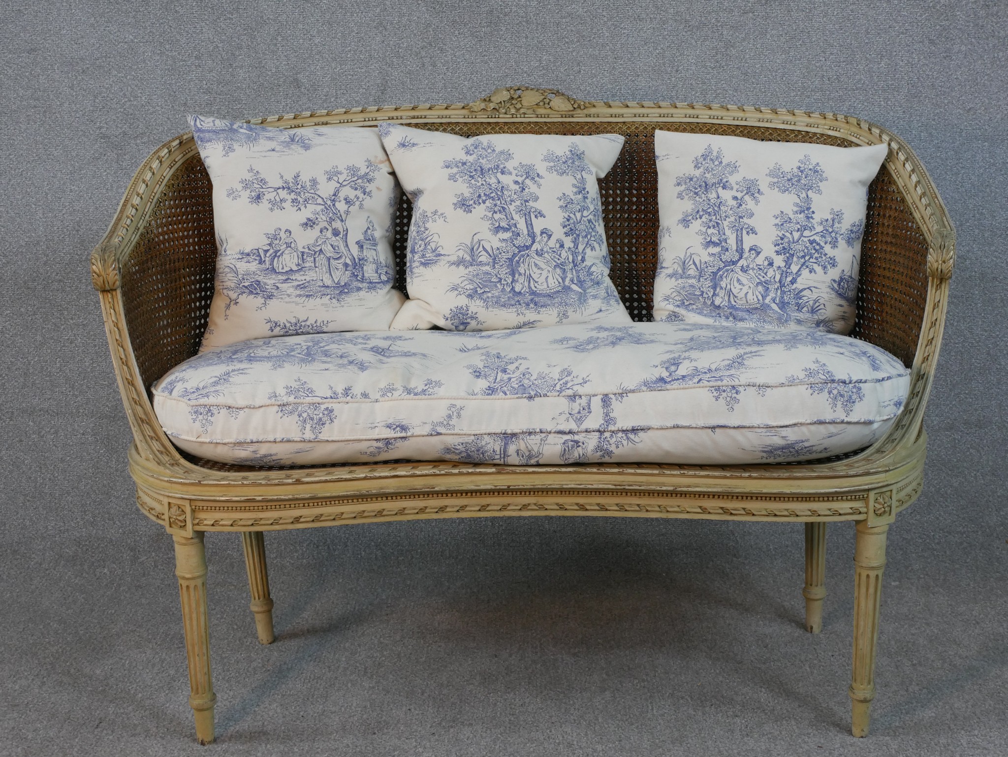 A French Louis XVI style painted canape sofa, with double caned back and sides, and loose cushions