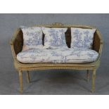 A French Louis XVI style painted canape sofa, with double caned back and sides, and loose cushions