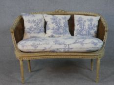 A French Louis XVI style painted canape sofa, with double caned back and sides, and loose cushions