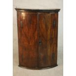 An 18th century bow front corner cabinet, with two doors enclosing shelves and three short