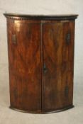 An 18th century bow front corner cabinet, with two doors enclosing shelves and three short