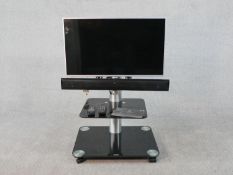 A Kitsound Ovation Slim Soundbar and TV on black glass and chrome stand, with manual and remote