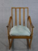 A mid 20th century beech rocking chair, with a spindle back and a blue upholstered loose cushion, on