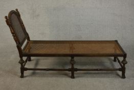 An early 20th century oak daybed in 17th century style, with a caned back and seat, the carved
