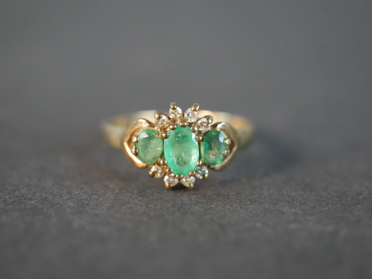 A 9 carat yellow gold emerald and diamond three stone ring, set with three oval mixed cut emeralds