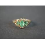 A 9 carat yellow gold emerald and diamond three stone ring, set with three oval mixed cut emeralds