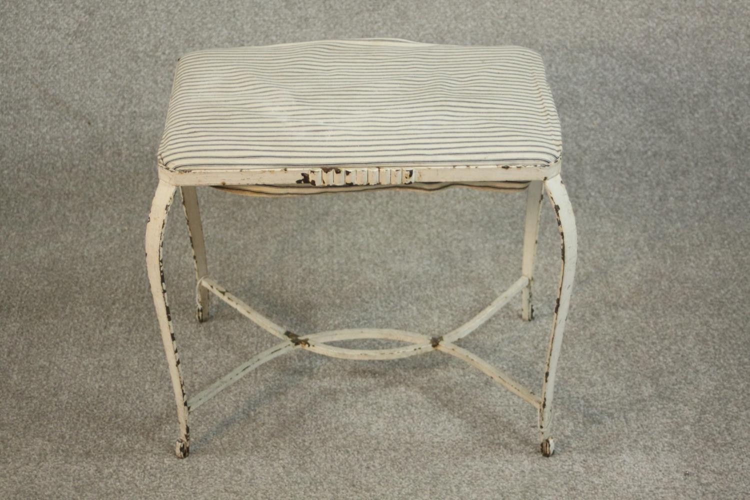 A white painted wrought iron stool, probably French, the seat upholstered in striped black and white