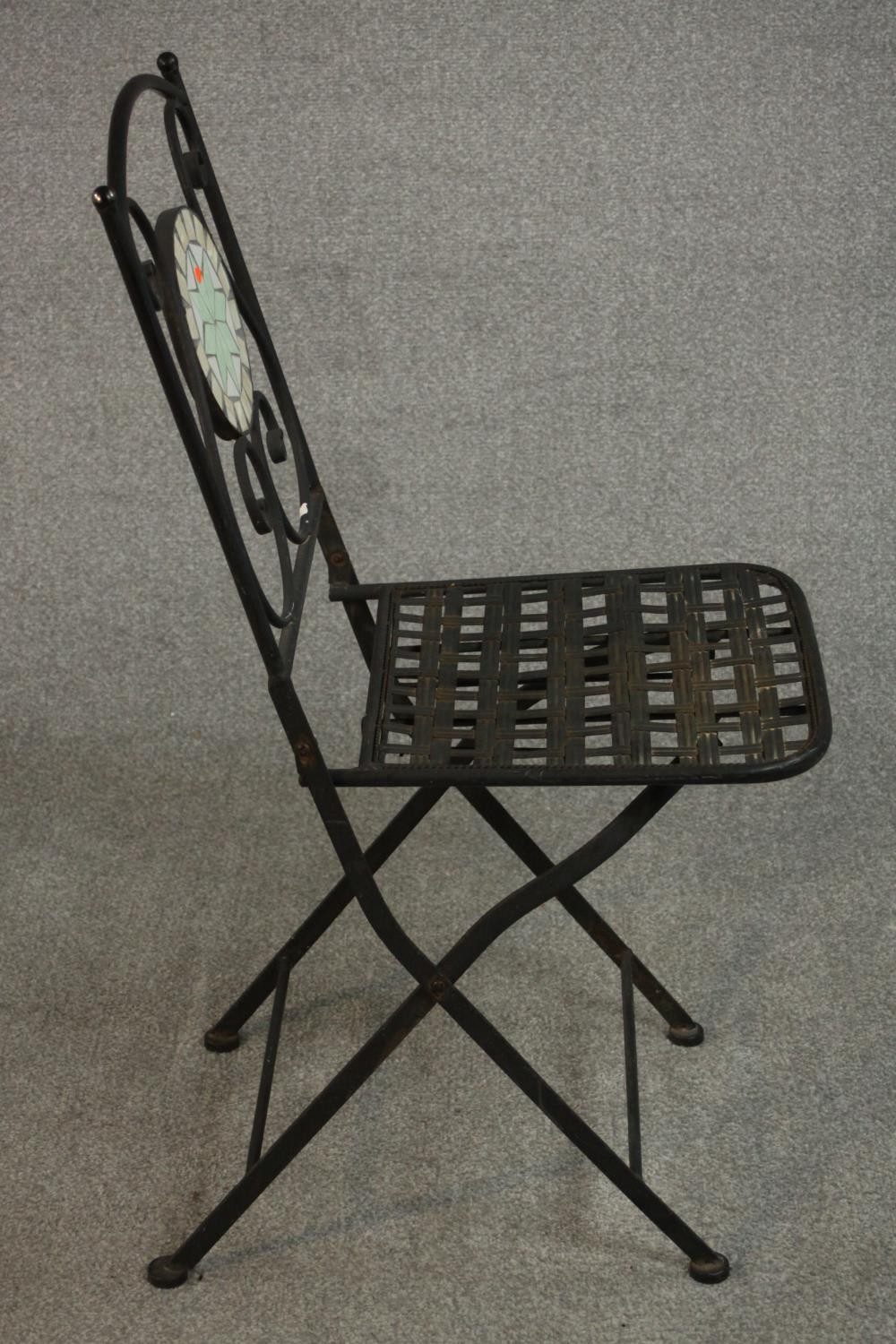 A wrought iron folding chair, the back with circular mosaic, over a slatted seat.