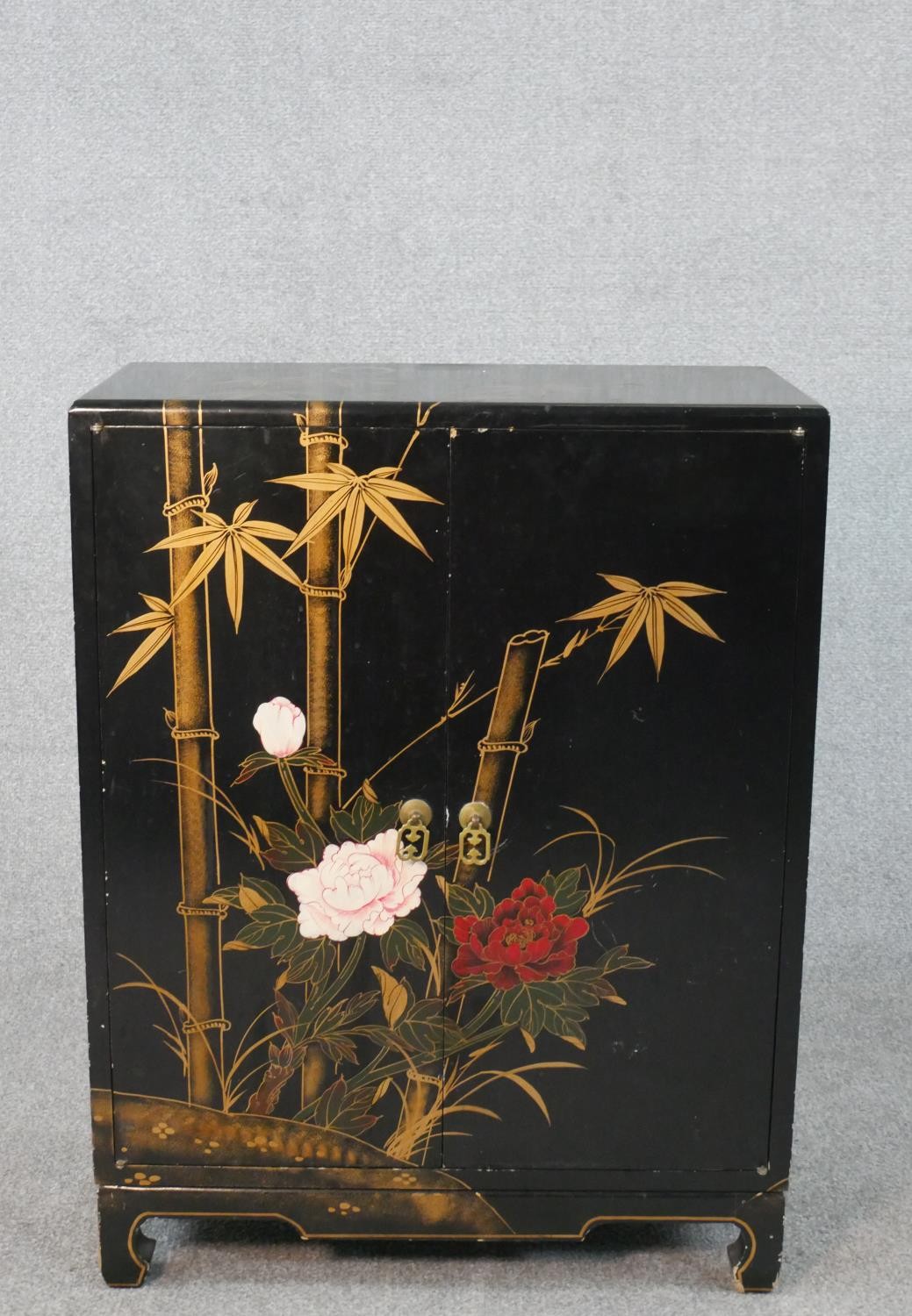 A Chinese peony and bamboo design black lacquered and gilt cabinet with two doors and three