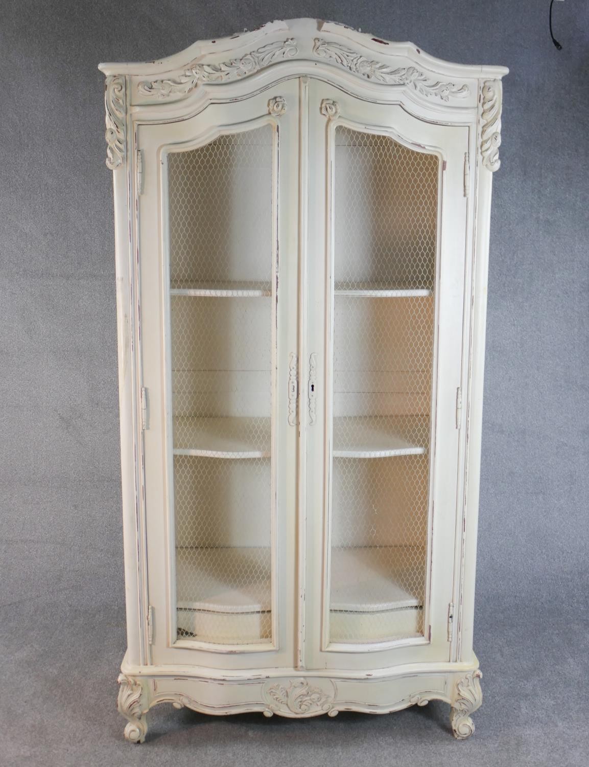 A French white painted and distressed bibliotheque, the carved cornice over two doors with mesh