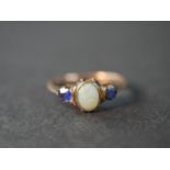 A pink metal (test as 9ct) opal and sapphire three stone ring, set to centre with an oval cabochon