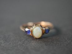 A pink metal (test as 9ct) opal and sapphire three stone ring, set to centre with an oval cabochon