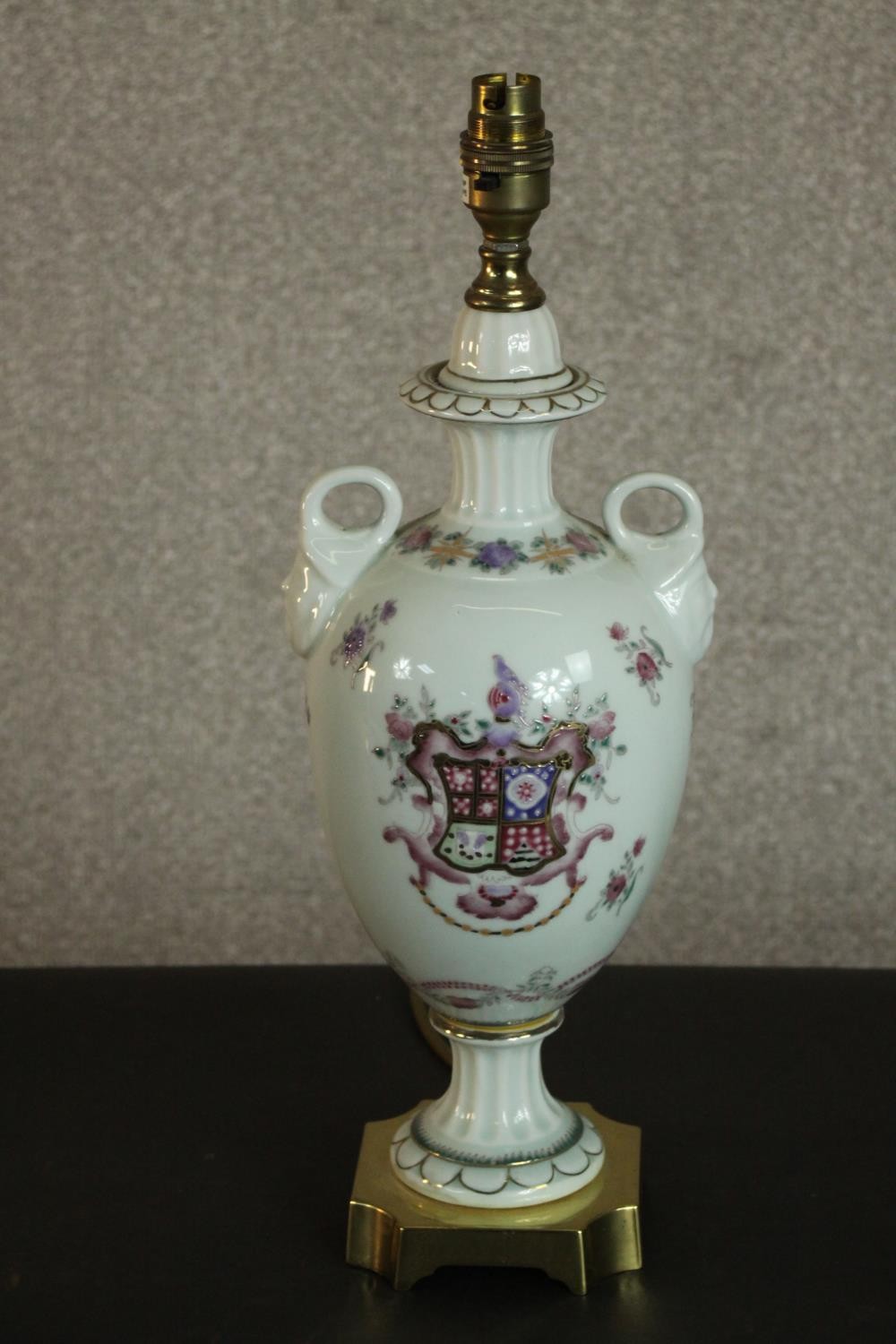 A hand painted armorial crest porcelain twin handled urn lamp with gilded detailing to the square
