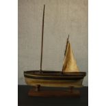 A scratch built painted wood pond yacht, named Doris, with a single sail, on a wooden stand. H.99