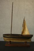 A scratch built painted wood pond yacht, named Doris, with a single sail, on a wooden stand. H.99