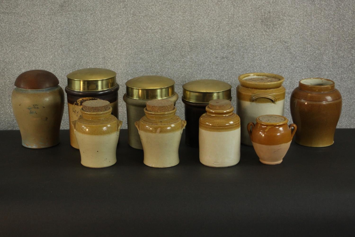 A collection of early 20th century honey glaze earthenware food storage jars, three with brass lids.