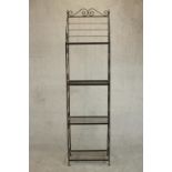 A wrought iron baker's rack of slender form, with four shelves, the sides with S shaped scrolling