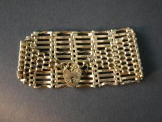 A 1970's 9ct yellow gold wide gate link bracelet with heart padlock charm and safety chain. The