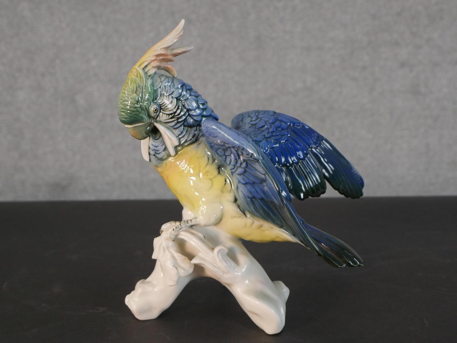 A Karl Ens porcelain blue and yellow parrot perched on a leafy branch, blue printed factory mark