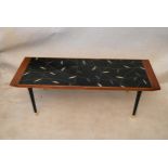 A 1950's teak coffee table, rectangular with a black glazed panel decorated with leaves, on black