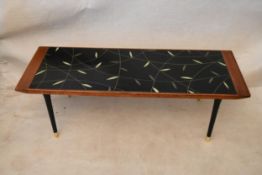 A 1950's teak coffee table, rectangular with a black glazed panel decorated with leaves, on black