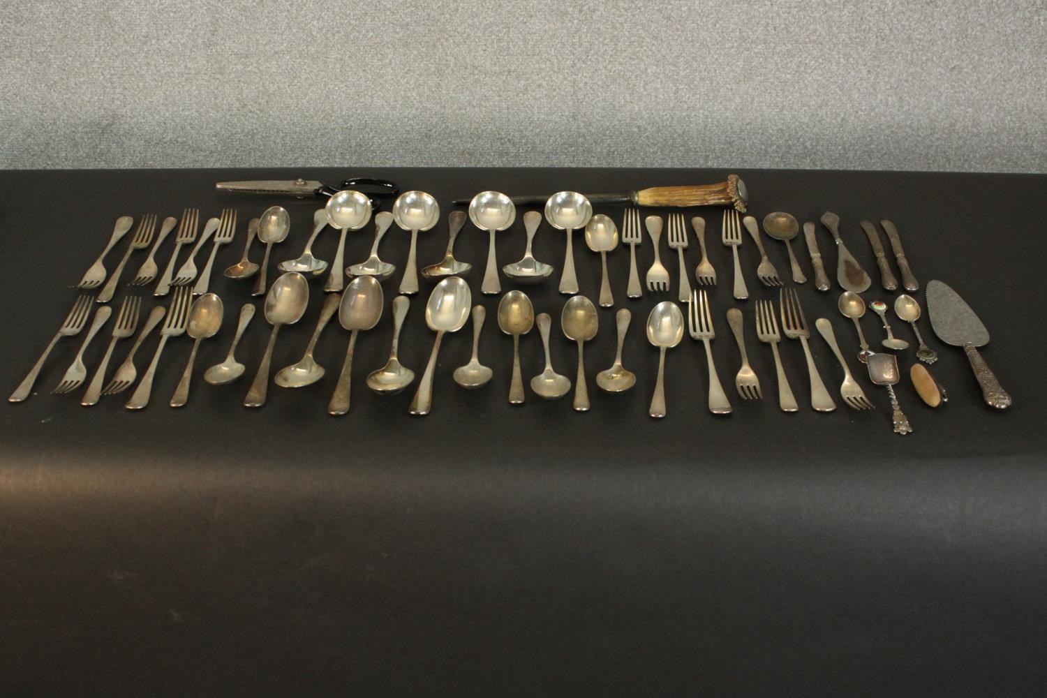 A collection of various silver plate cutlery, including a knife sharpener with antler handle, shoe