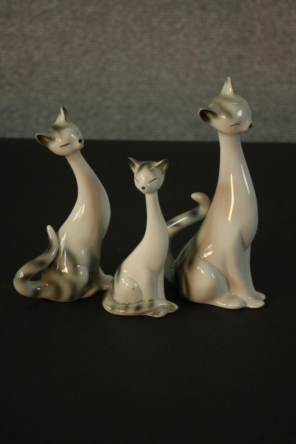 Three German porcelain Siamese cats in three different sizes, makers mark to base. H.18 W.9 D.7cm.