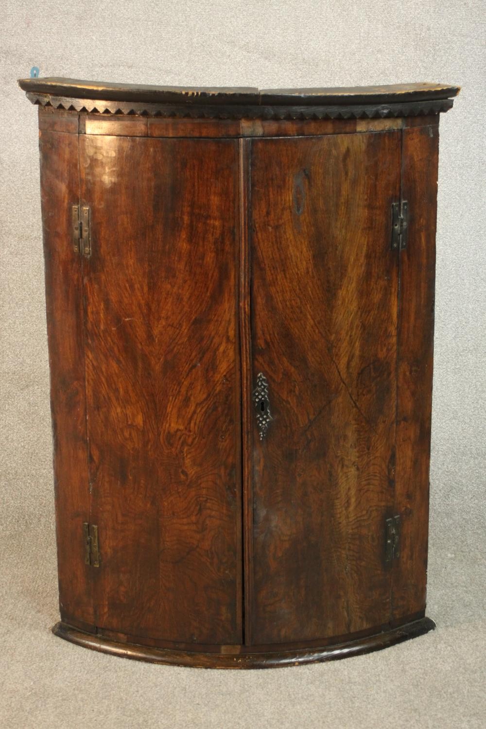An 18th century bow front corner cabinet, with two doors enclosing shelves and three short