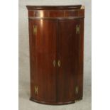 An 18th century mahogany bow front corner cabinet, the two cupboard doors with brass butterfly