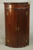 An 18th century mahogany bow front corner cabinet, the two cupboard doors with brass butterfly