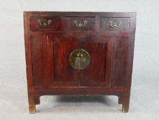 A Chinese stained pine side cabinet, with three short drawers over a pair of cupboard doors
