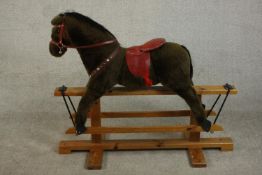 A child's rocking horse, upholstered in brown hair, with a red leather saddle and reins, on a pine