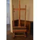 A beech adjustable studio easel with H frame on sled supports resting on casters. H.185cm.