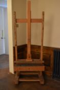 A beech adjustable studio easel with H frame on sled supports resting on casters. H.185cm.