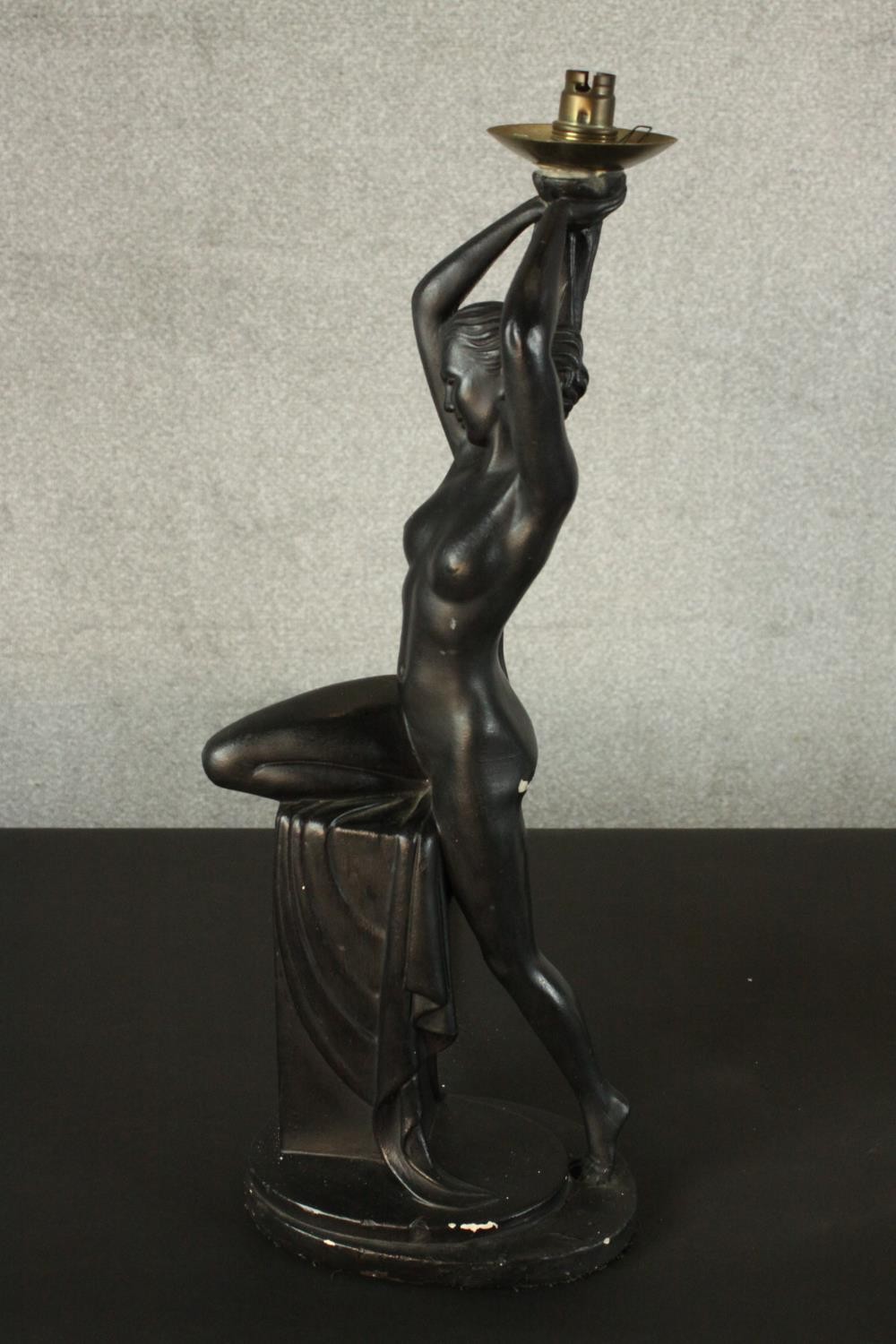 An Art Deco style black painted plaster table lamp in the form of a nude dancer perched on a