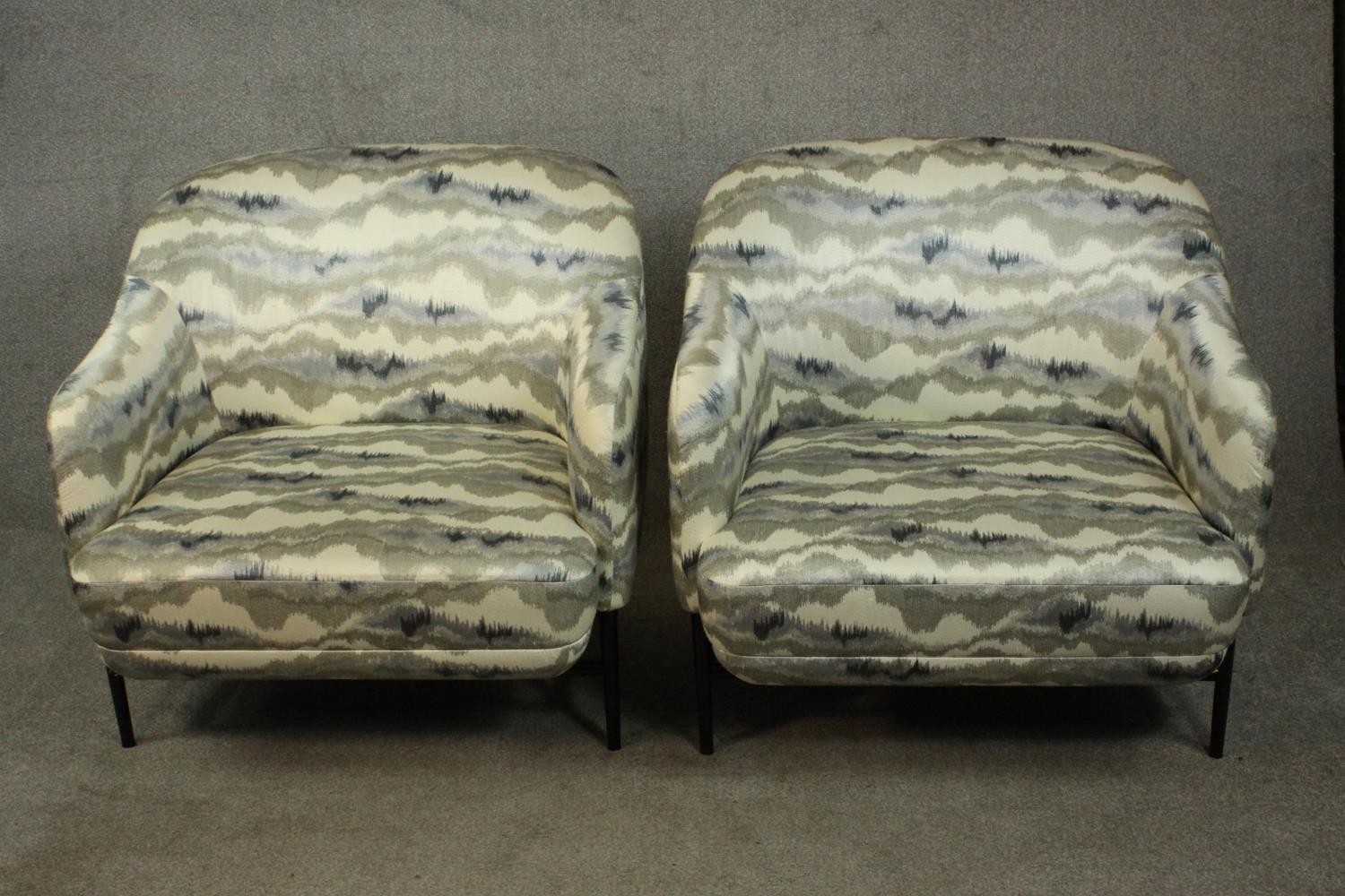 A pair of retro styled armchairs, with patterned upholstery in hues of grey, on a black powder