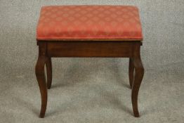 A circa 1890 walnut piano stool, the seat upholstered in pink fabric, rising to reveal storage