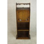 An early 20th century oak drinks cabinet, with a glasses rack over a cupboard door above shelves.