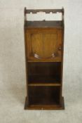 An early 20th century oak drinks cabinet, with a glasses rack over a cupboard door above shelves.