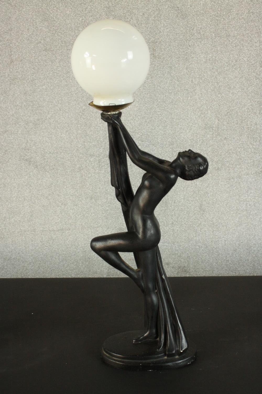 An Art Deco style black resin table lamp in the form of a nude dancer with white glass globe