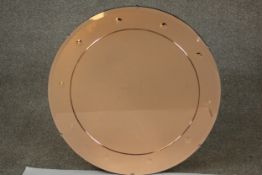 A circular peach mirrored glass mirror, the frame with a bevelled edge and spherical decoration.