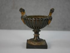 A 19th century gilded twin handled gadrooned form urn with foliate motifs on a square base. H.13.5