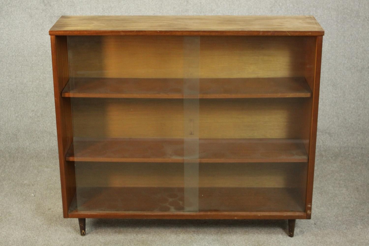 A circa 1960s Jonell bookcase, with a pair of glass sliding doors enclosing shelves, on tapering