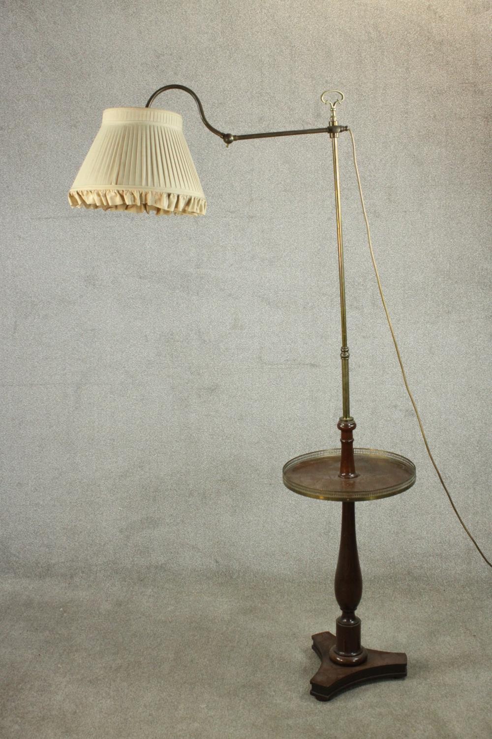 An adjustable standard lamp, with a brass arm and stem, over a circular tier with a pierced brass